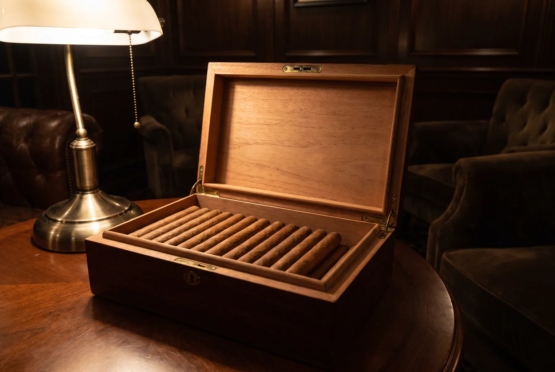 An open cedar humidor of cigars beside a brass lamp